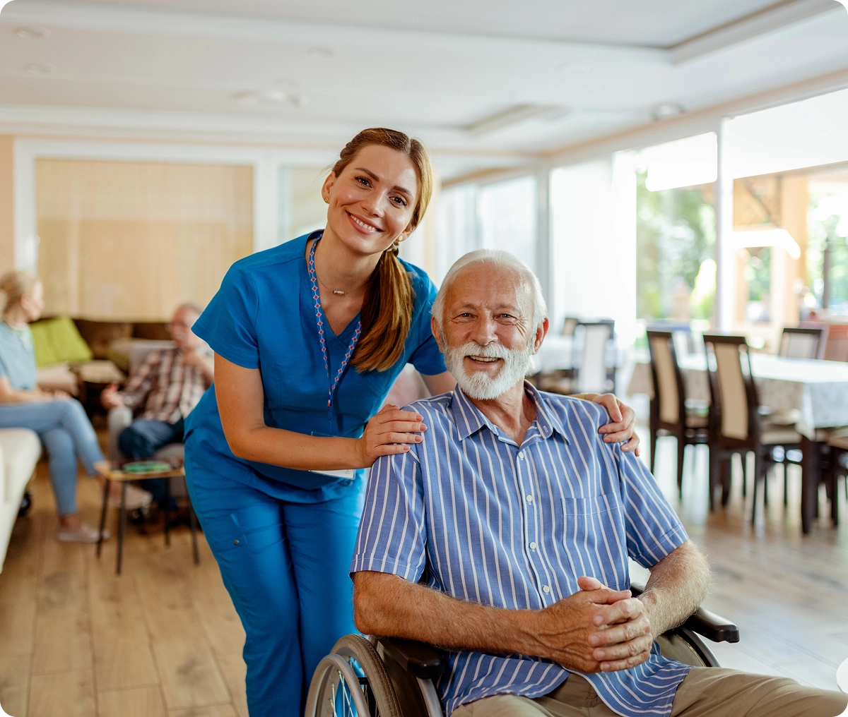 Caregiver smiling with elderly man in wheelchair.