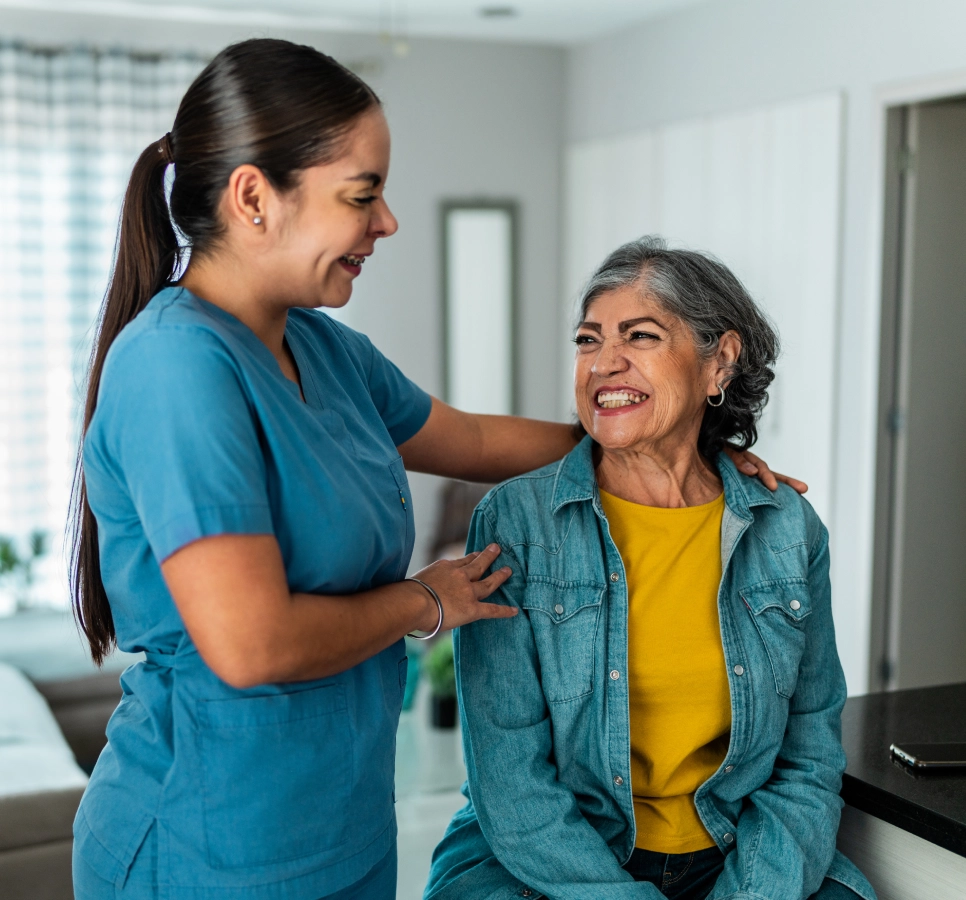 Caregiver smiling with elderly woman at home.