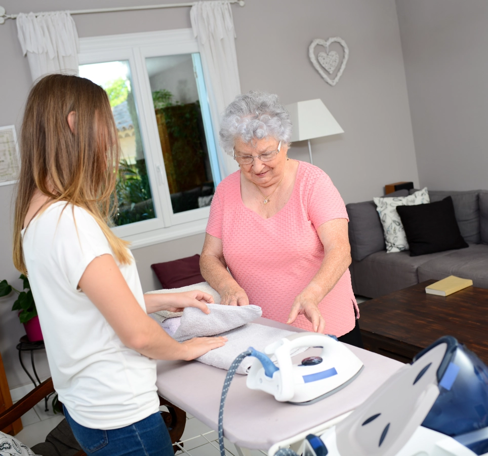 Elderly woman and young girl ironing clothes.